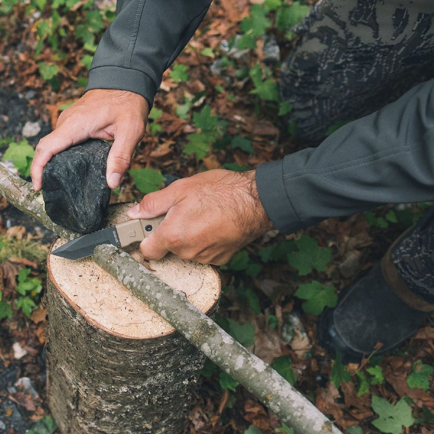 Gear Aid Kotu Coyote Knife being used to cut a thin branch outdoors probably for fire kindling