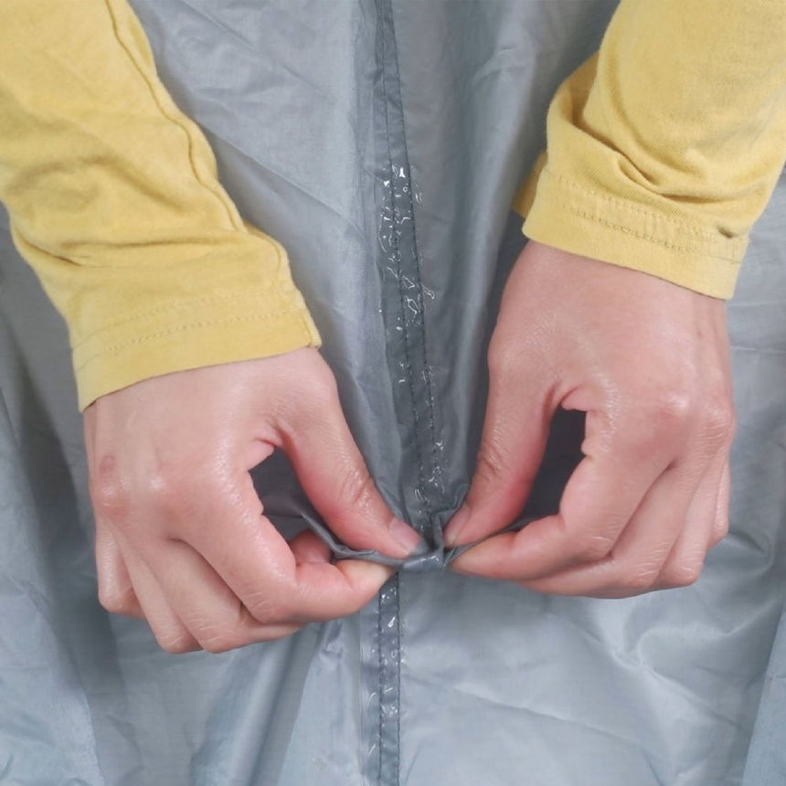 Gear Aid Seam Grip+ SIL Silicone Tent Sealant has been applied to a seam on a grey tent. User is testing the repair of the seam on the grey tent.