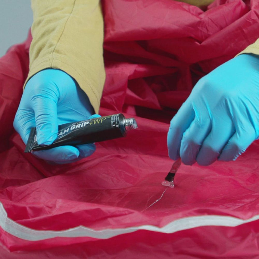 Gear Aid Seam Grip WP+ Adhesive and Sealant being applied with the application brush to a tear in a red tent