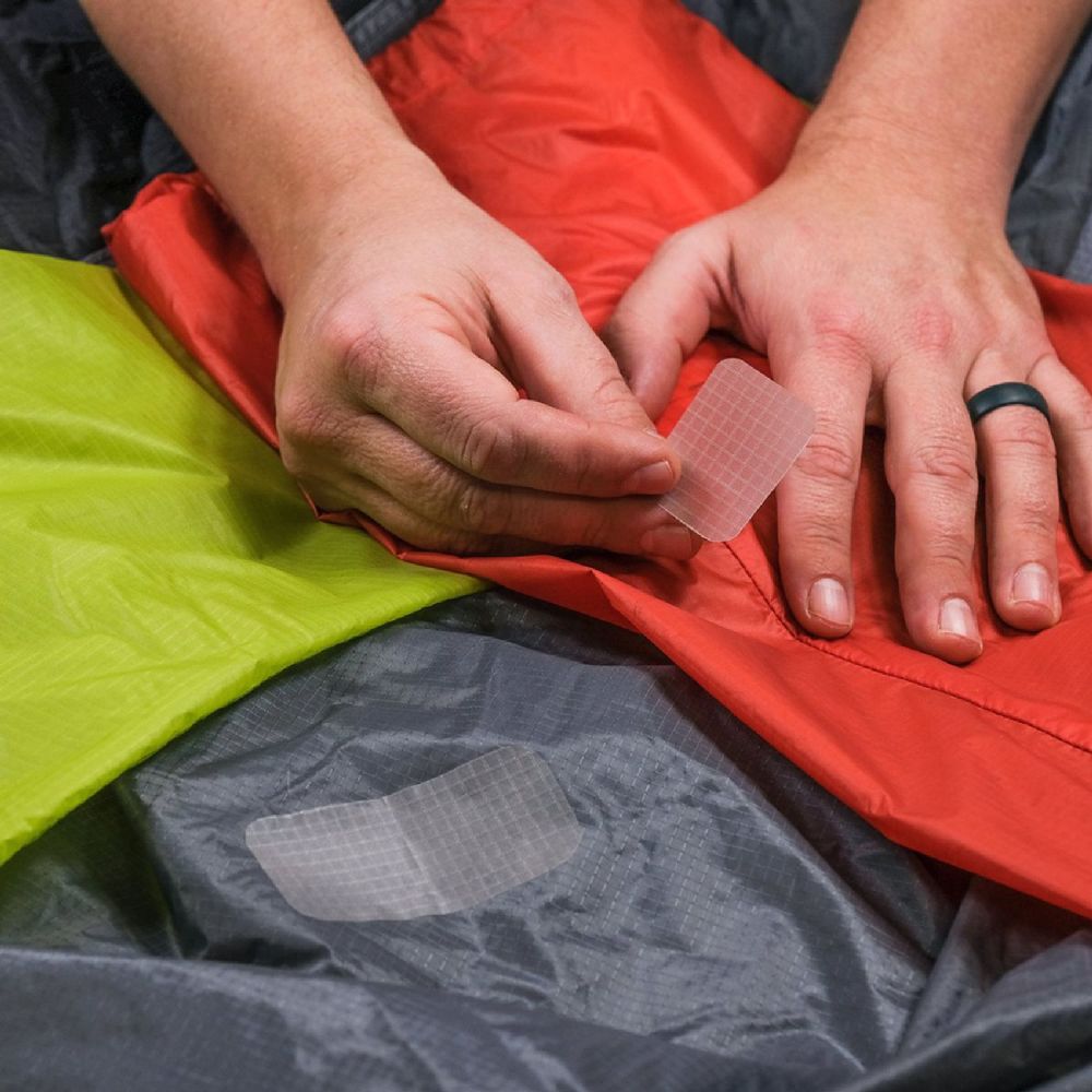 Hand model sticking Semi Transparent Peel and Stick Gear Aid Tenacious Tape Sil Nylon Repair Patch to tear in an a jacket