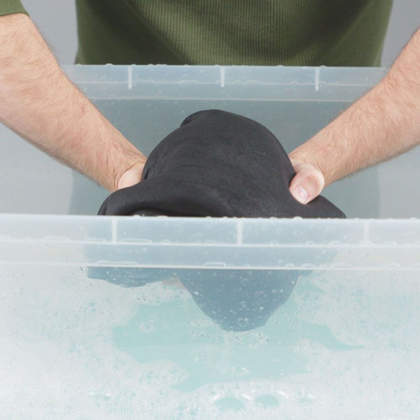 Hand model putting neoprene suit in a transparent basin with Gear Aid Revivex Wetsuit Shampoo diluted in water