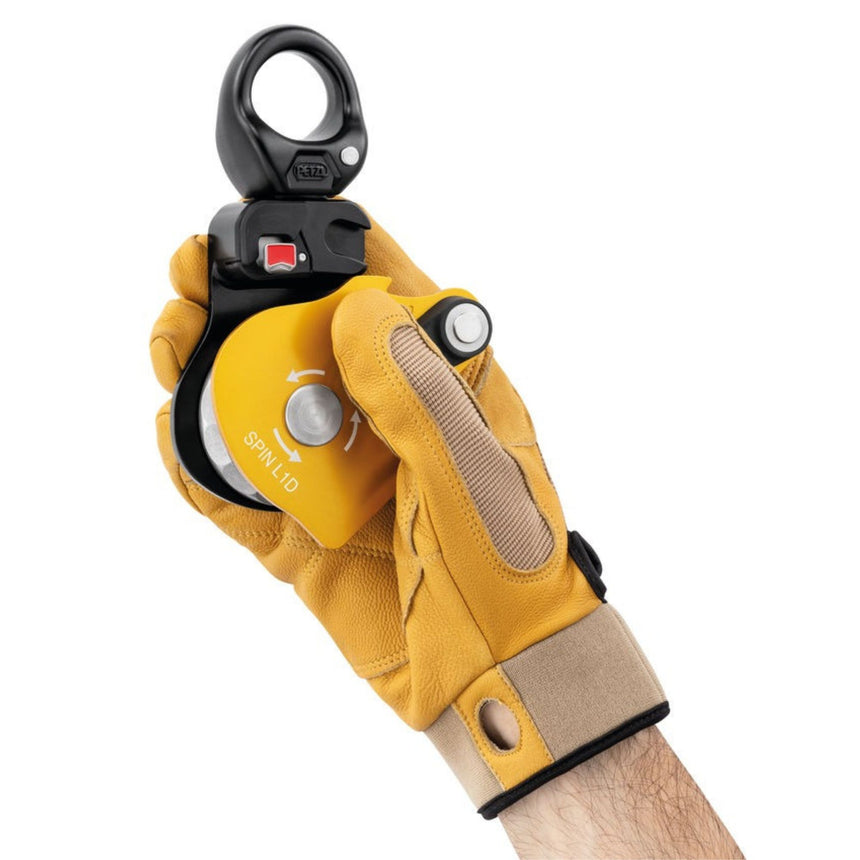 Professional wearing a glove holding an open Petzl Spin L1D single pulley with one-way rotation and swivel