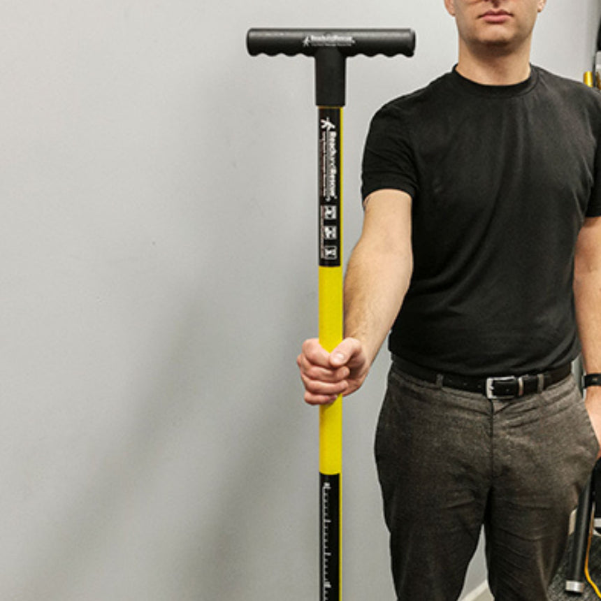 A professional holding a Reach and Rescue search pole, highlighting its ergonomic T-bar handle and yellow fiberglass shaft with measurement markings.