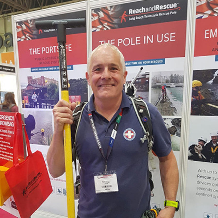 A rescue professional showcasing the Reach and Rescue Wading Pole at Reach and Rescue exhibition booth, with informational banners about the product displayed in the background.