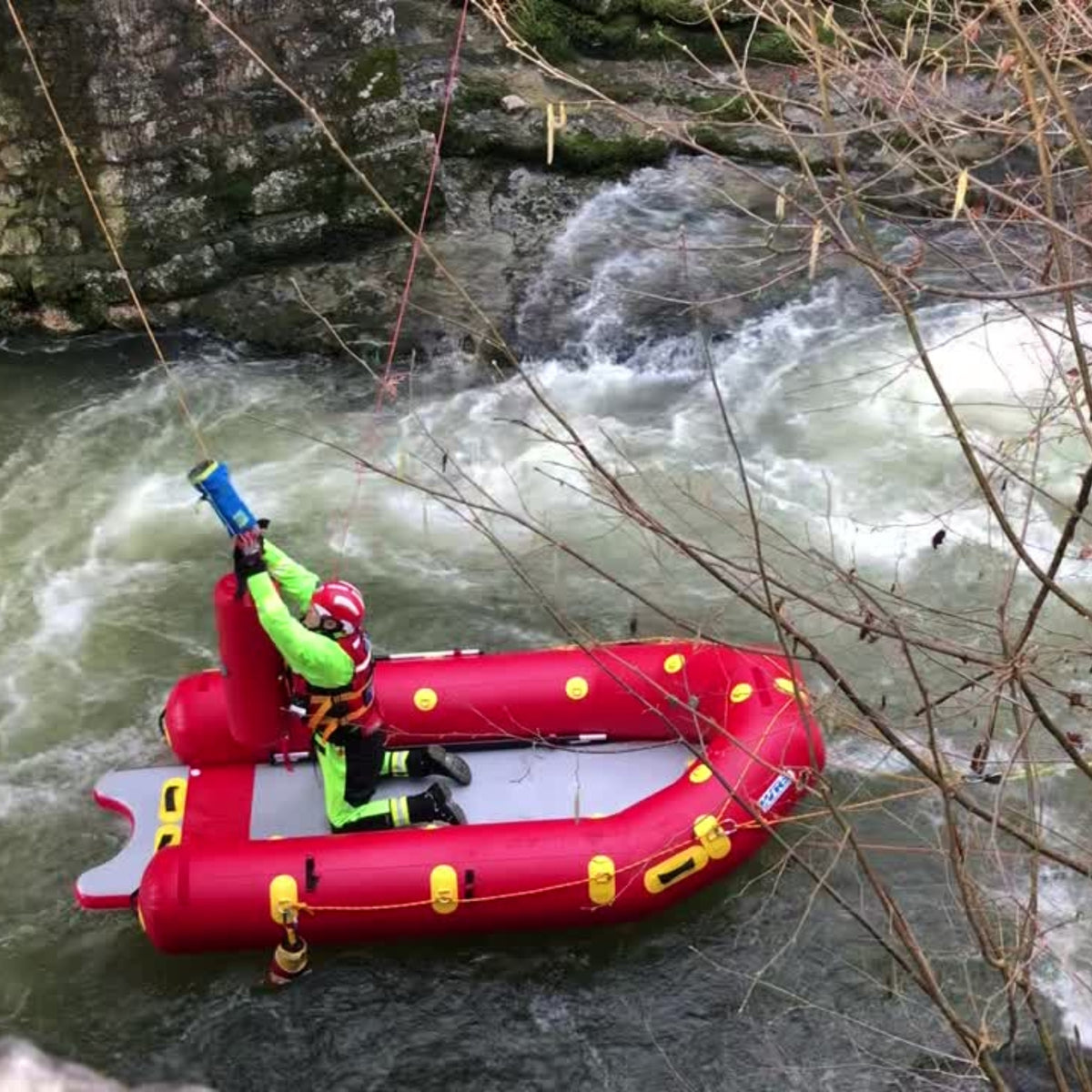 Rescue responder kneeling in Mega Sled with hands in the air reaching for thowline. The Mega Sled is attached to ropes on a whitewater river