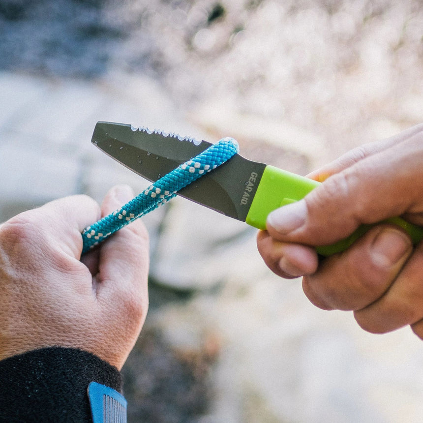 Hand model demonstrating Green Gear Aid Akua River Knife about to cut a blue cord 