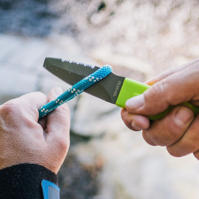 Hand model demonstrating Green Gear Aid Akua River Knife about to cut a blue cord 