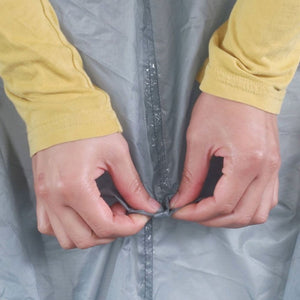Gear Aid Seam Grip+ SIL Silicone Tent Sealant has been applied to a seam on a grey tent. User is testing the repair of the seam on the grey tent. 