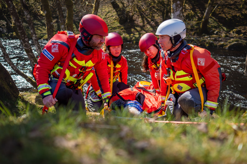 Rescue team assisting a casualty beside a river.