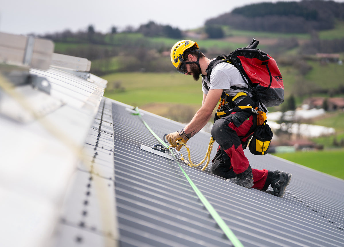 Roofer wearing a helmet and harness while working on a metal roof.