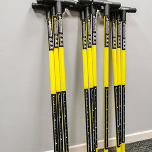 A set of Reach and Rescue search poles neatly stacked against a grey wall, showcasing the yellow fiberglass shafts and ergonomic black T-bar handles