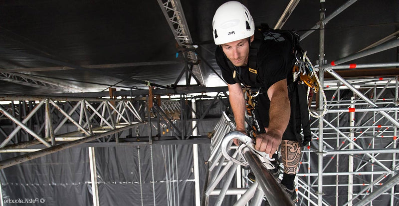 Stage rigger wearing a helmet and harness while working on lighting truss.